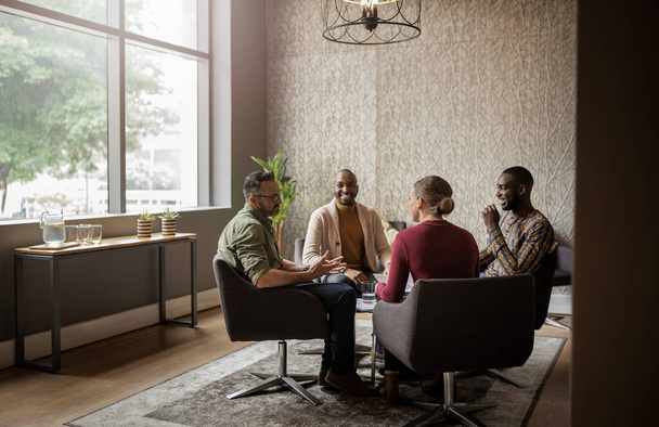 Diverse group of businesspeople smiling and talking together during a casual meeting in an office lounge area - Photo, Image