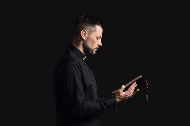 Handsome priest with Bible on dark background - Fotoğraf, Görsel