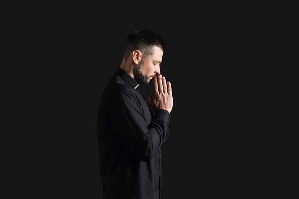 Handsome praying priest on dark background - Zdjęcie, obraz