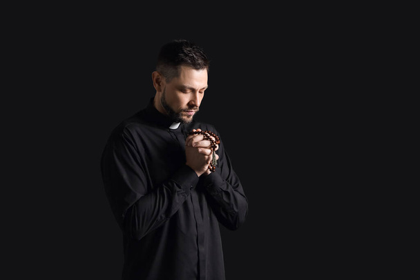 Handsome praying priest on dark background - Photo, Image