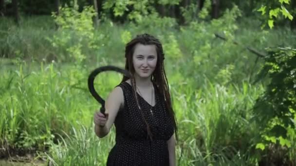 Energetisch jong meisje met dreadlocks staat in het bos en houdt in haar handen een sikkel scherp tillen en laten zakken. Close-up - Video