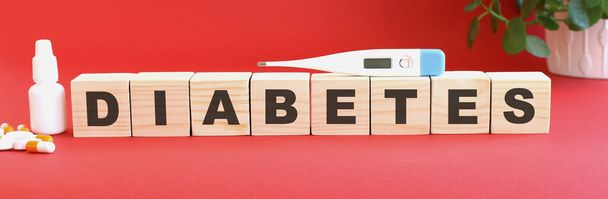 The words DIABETESis made of wooden cubes on a red background with medical drugs. Medical concept. - Photo, Image