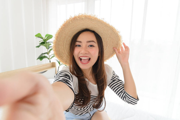 Retrato de jovem mulher asiática no verão roupas casuais e chapéu de palha segurando telefone inteligente enquanto vídeo-chamada ou tirar selfie na câmera frontal
 - Foto, Imagem