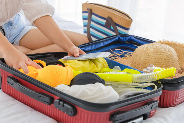 Close-up female hands packing summer clothes and beach accessories into suitcases on bed. Preparing travel items for new journey. summer holidays, vacation concept. - 写真・画像