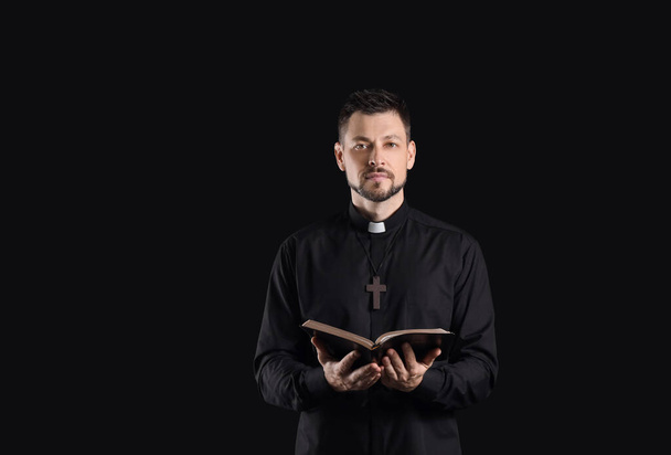 Knappe priester met bijbel op donkere achtergrond - Foto, afbeelding