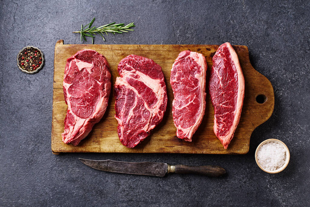 cutting board with ribeye and striploin with picanha and chuck roll  fresh black angus prime raw beef steaks on wooden background, top view - Foto, Bild