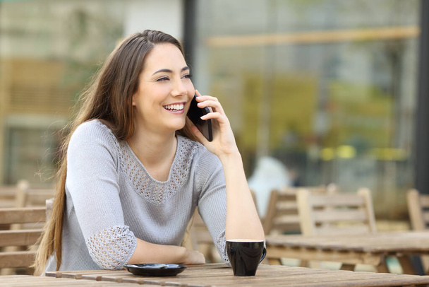 Happy woman calling on smart phone sitting in a coffee shop terrace table - Foto, Imagem