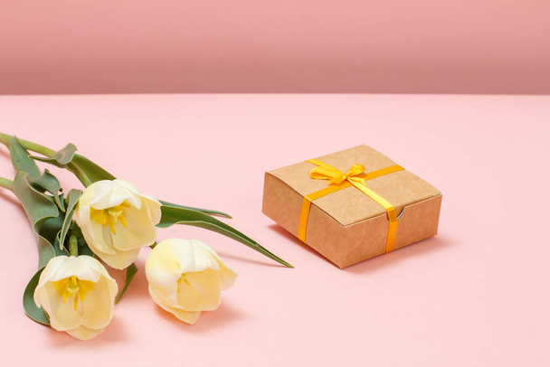 Lahjapakkaus, jossa kauniit keltaiset tulppaanit vaaleanpunaisella taustalla. Huippunäkymä. Lahjan antamisen käsite lomilla. - Valokuva, kuva