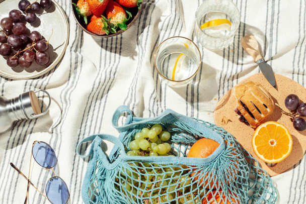 Plato de picnic de verano, frutas, bayas y agua de limón en manta de algodón rayado
 - Foto, imagen