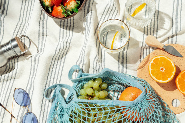 Summer picnic flatlay, fruits, berries and lemon water on striped cotton blanke - Photo, image