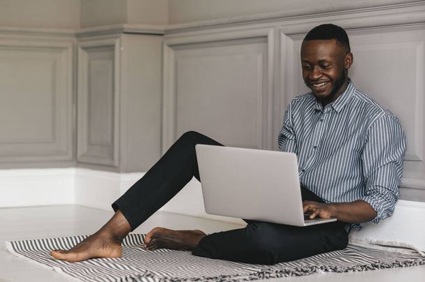 black young man sitting on the floor with a laptop and working - Foto, imagen