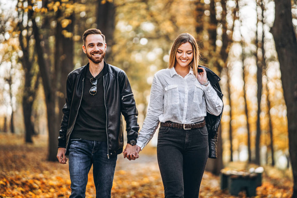 Retrato de una feliz pareja que camina al aire libre en el parque de otoño. Hombre y mujer tomados de la mano y oliendo
. - Foto, imagen