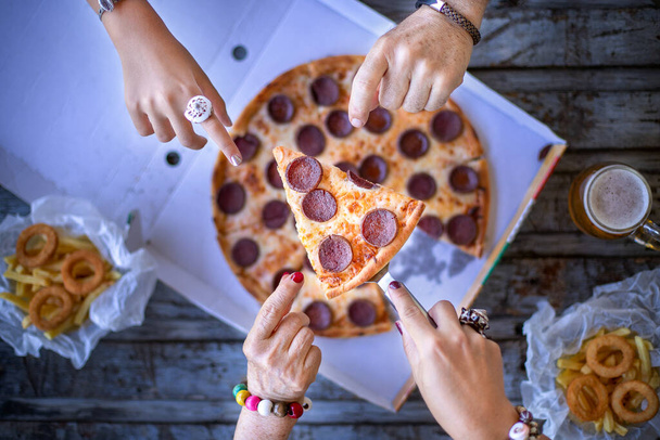 Masada bir sürü el var ve bu arkadaşlar masada pizza yiyorlar. Pepperonili pizza ile fast food konsepti. - Fotoğraf, Görsel