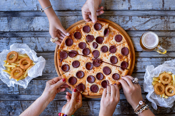 Many hands on the table and these friends are eating pizza on the table. Fast food concept with pepperoni pizza. - Foto, Imagem
