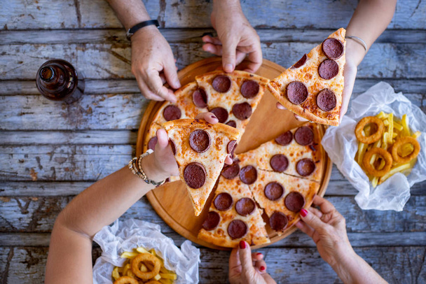 Molte mani sul tavolo e questi amici stanno mangiando pizza sul tavolo. Fast food con pizza al salame piccante. - Foto, immagini