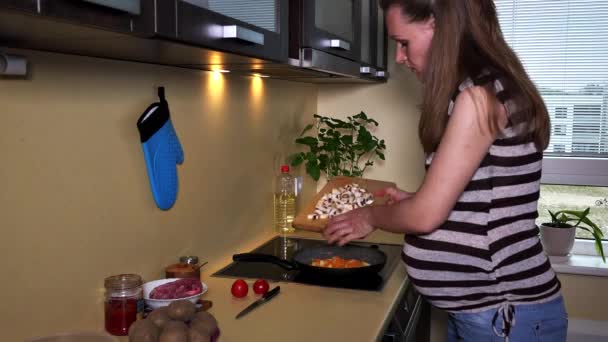 Pregnant woman put cut champion mushrooms into cooking pan on hob - Footage, Video