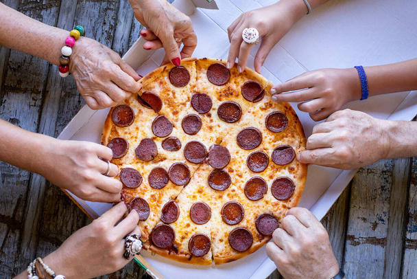 Monet kädet pöydällä ja nämä ystävät syövät pizzaa pöydällä. Pikaruoka käsite pepperoni pizza. - Valokuva, kuva