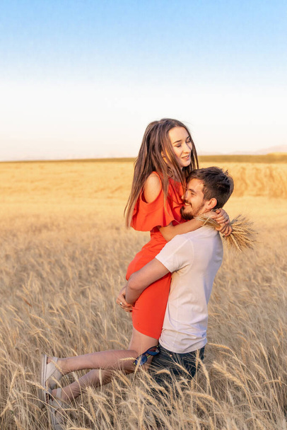 Muž drží svou krásnou přítelkyni ve zbrani, zatímco stojí na pšeničném poli - Fotografie, Obrázek