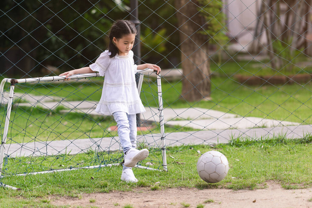 aasialainen söpö vauva tyttö yllään valkoinen paita pelaa jalkapalloa kentällä iloisesti. - Valokuva, kuva