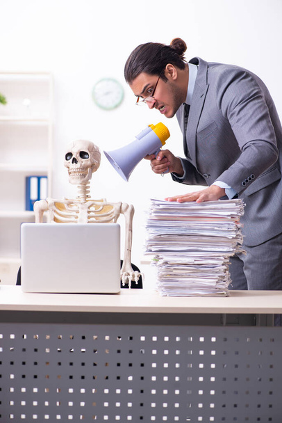 Fiatal férfi alkalmazott és csontváz az irodában - Fotó, kép