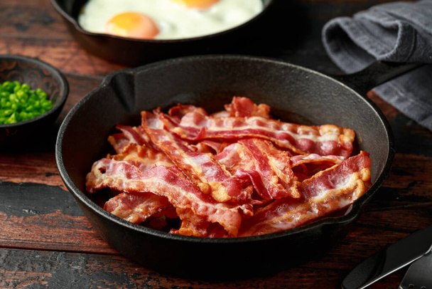 Fried crunchy Streaky Bacon pieces in a cast iron skillet - Photo, image