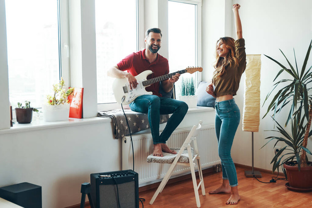 Playful young couple in casual clothing bonding together and smiling while playing the guitar      - 写真・画像