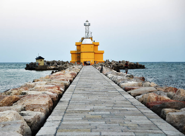Italia, bellissimo faro giallo sul Mar Mediterraneo, pontile in pietra con pescatori - Foto, immagini