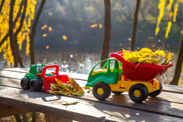 Piccolo camion giocattolo e trattore si erge su una superficie di legno sullo sfondo di un parco autunnale sfocato. - Foto, immagini
