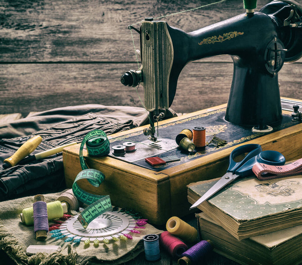 Old sewing machine and accessories for sewing, scissors, needles and tailor tape on the table. The concept of sewing accessories. Retro toning - Фото, зображення