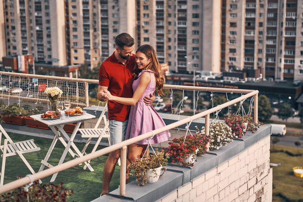 Beautiful young couple in casual clothing dancing and smiling while having romantic dinner on the rooftop patio outdoors - Valokuva, kuva