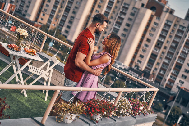 Loving young couple in casual clothing dancing and smiling while having romantic dinner on the rooftop patio outdoors - Фото, зображення
