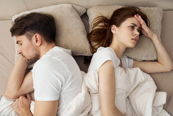 Μια αναστατωμένη γυναίκα ξαπλώνει στο κρεβάτι και ο άντρας δίπλα της - Φωτογραφία, εικόνα