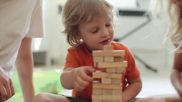 Les enfants jouent le puzzle et le petit garçon rit de la construction en ruine des blocs de bois. Gros plan - Séquence, vidéo