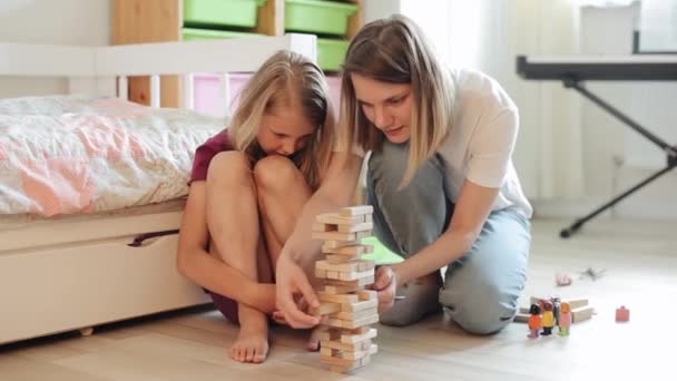 Mãe e filha brincam na sala em um quebra-cabeça cuidadosamente puxando blocos de madeira para fora da construção. Close-up
 - Filmagem, Vídeo