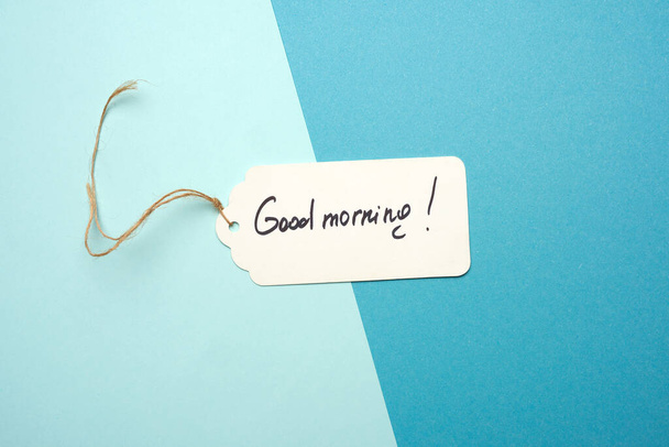 λευκή χάρτινη ετικέτα με καφέ σχοινί και την επιγραφή καλημέρα, μπλε φόντο - Φωτογραφία, εικόνα