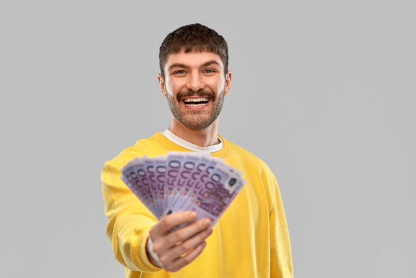 smiling young man in yellow sweatshirt with money - Фото, зображення