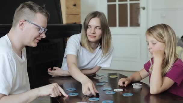 Long-haired little girl enthusiastically plays a board game Memo with adults sitting at a table in the room. Close-up - Footage, Video