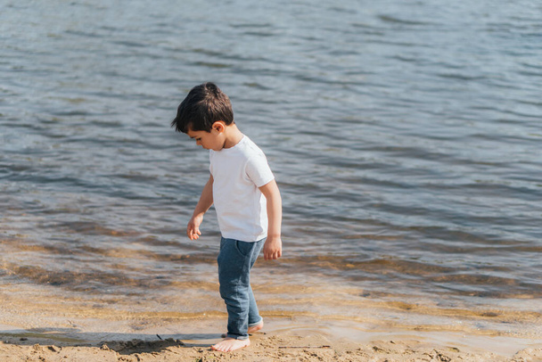 aranyos fiú farmerban álló kék tó mellett  - Fotó, kép