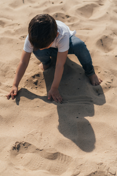 high angle view of boy sitting and touching sand  - Photo, Image
