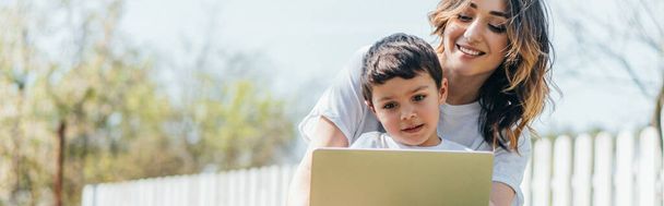 horizontal concept of happy mother and son using laptop outside - Foto, imagen