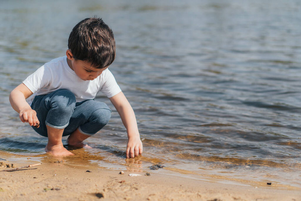 cute boy sitting in water and touching wet sand - Photo, Image