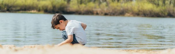 池の近くに座ってる可愛い男の子のパノラマ写真  - 写真・画像