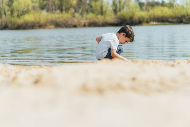 池の近くに座っている可愛い少年の  - 写真・画像