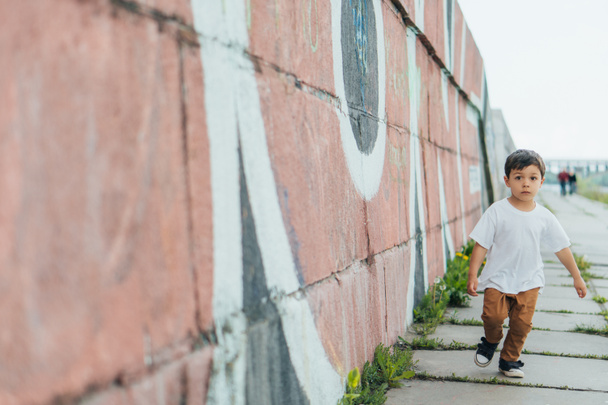 επιλεκτική εστίαση του χαριτωμένο αγόρι τρέχει κοντά στον τοίχο με γκράφιτι  - Φωτογραφία, εικόνα