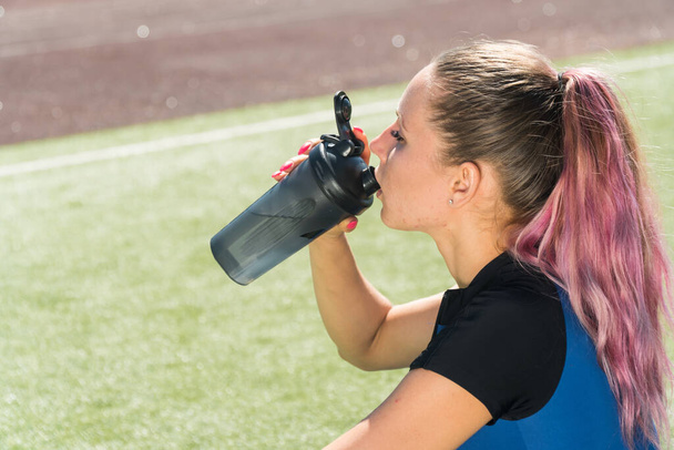 Portrait of a sports girl who drinks from a shaker against the backdrop of beautiful nature on a sunny summer day - Foto, Imagem