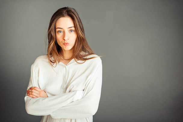 Young girl in a white shirt on a gray background. French woman in white blouse against a background of gray walls. Without retouching. - Photo, Image