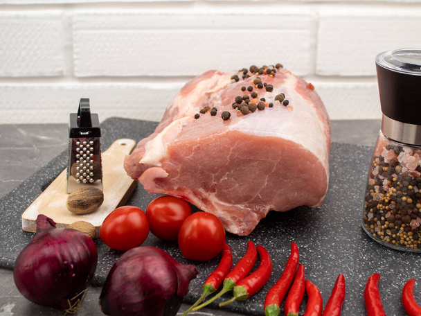Ωμό χοιρινό κρέας σε μαρμάρινο πίνακα με μπαχαρικά και λαχανικά - Φωτογραφία, εικόνα