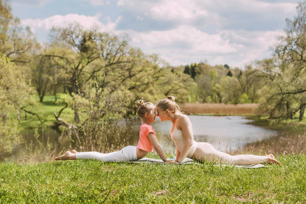Uma bela jovem com sua encantadora filha adolescente pratica ioga ao ar livre em um parque. Vista lateral, espaço para texto
 - Foto, Imagem