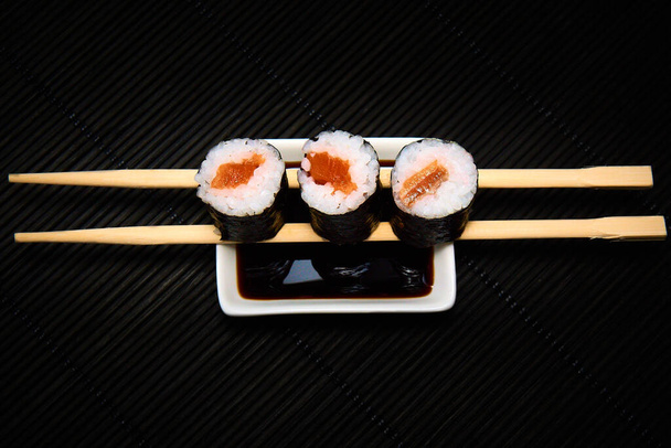 Three pieces of syake maki roll lying on sticks on a black background - Photo, Image