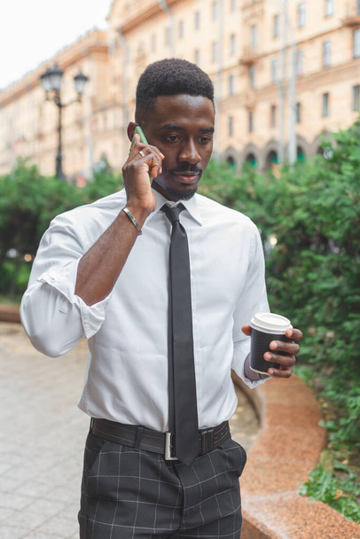 Hombre de negocios negro americano en un apuro. Un hombre con café para llevar hablando por teléfono a toda prisa. Gran ritmo de la ciudad - Foto, imagen